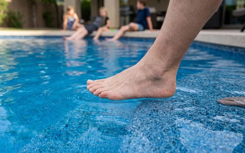 Foot entering pool water on Pebble Tec — textured feel